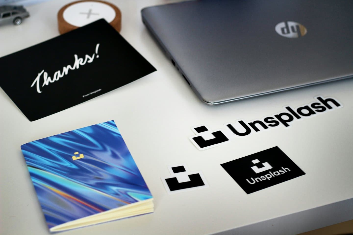 Naklejki na laptopa z logo i notatniki ułożone na białym biurku.